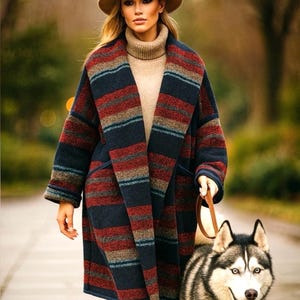 May include: A long, striped coat in navy, red, and tan worn with a tan turtleneck and hat. The coat has a wide collar and is paired with blue jeans. A husky dog is on a leash.