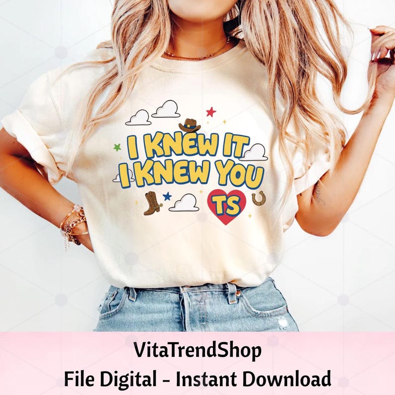 May include: A cream-colored t-shirt featuring the text I KNEW IT I KNEW YOU TS in blue and yellow letters. The design includes illustrations of a brown cowboy hat, a brown cowboy boot, a horseshoe, white clouds, and a red heart with the letters TS.