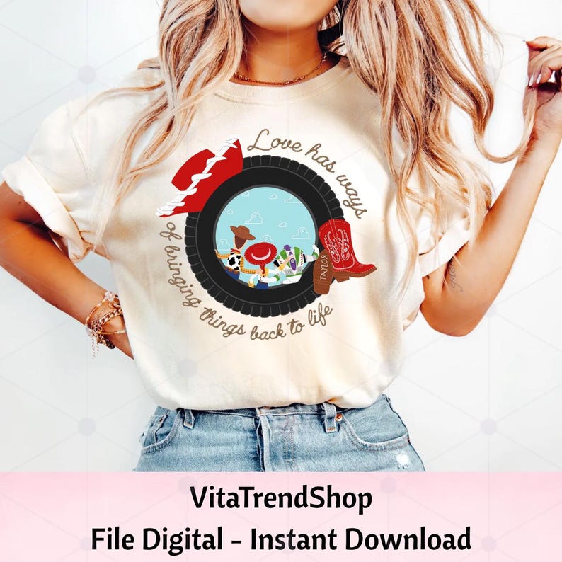 May include: A cream-colored t-shirt featuring a graphic of a black tire framing a scene with cartoon characters, a red cowboy hat, and a red cowboy boot. The text reads, Love has ways of bringing things back to life, with the name Taylor on the boot.