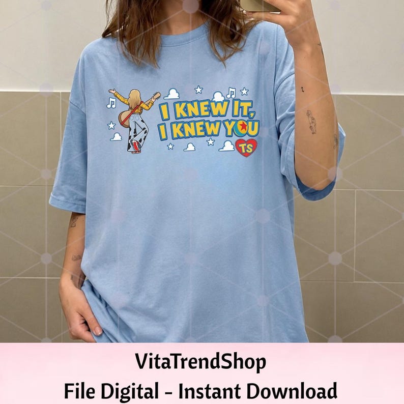 Pu&ograve; includere: Una t-shirt azzurra con la grafica di una persona che suona la chitarra, circondata da nuvole, stelle e note musicali. Il testo recita I KNEW IT, I KNEW YOU con un cuore rosso contenente le lettere TS e una piccola icona di una palla.