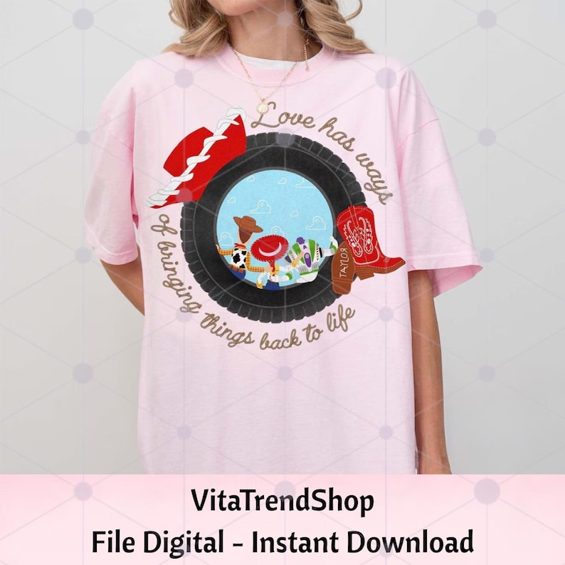 May include: A light pink t-shirt featuring a graphic of a black tire framing a blue sky scene with three cartoon characters. The design includes a red cowboy hat, a red cowboy boot, and the text Love has ways of bringing things back to life.