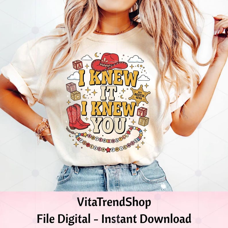 Pu&ograve; includere: Una t-shirt color crema con una stampa grafica che riporta il testo I KNEW IT I KNEW YOU. Il design include un cappello da cowboy rosso, stivali da cowboy rossi, blocchi dell'alfabeto, una stella da sceriffo con l'etichetta BESTIE 4EVA e una collana.