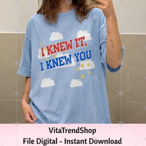 K&ouml;nnte beinhalten: Ein hellblaues T-Shirt mit kurzen &Auml;rmeln und einem Grafikdruck aus wei&szlig;en Wolken und gelben Sternen. Der Text "I KNEW IT, I KNEW YOU" ist mittig in roten und blauen Blockbuchstaben aufgedruckt. Das T-Shirt hat einen Rundhalsausschnitt und eine lockere Passform.