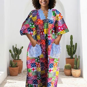 May include: A floor-length dress featuring a vibrant patchwork pattern of various colorful geometric and floral prints. The garment includes short sleeves, a scalloped light blue lace neckline, and two large light blue lace pockets on the front.
