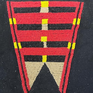 May include: A beaded decorative piece with a geometric design. The piece features red, black, yellow, and beige beads. The design includes horizontal stripes and a triangular bottom section, all set against a black background.