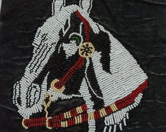 May include: A square black fabric panel featuring a detailed horse head portrait crafted from small white, black, red, and tan beads. The horse wears a beaded bridle with red and tan accents, and the design is centered on the dark textured background.