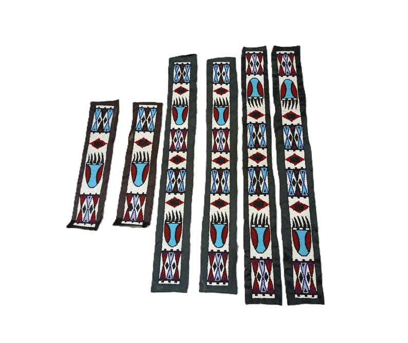 May include: Six long, narrow fabric strips featuring intricate beadwork in white, red, blue, and black. The pattern includes repeating geometric diamond shapes and stylized bear claw motifs. The strips vary in length and are arranged vertically.