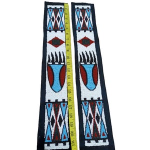 May include: Two long, rectangular strips of black fabric decorated with intricate white, red, black, and light blue beadwork in geometric and bear claw patterns. A yellow measuring tape placed between the strips shows a length of 22 inches.