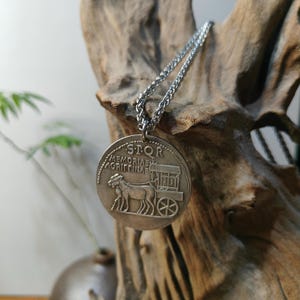 May include: A silver-toned circular pendant necklace featuring a relief design of a horse-drawn carriage. The coin-style charm is engraved with the text SPQR and MEMORIAE AGRIPPINAE, suspended from a matching silver-toned metal chain link necklace.
