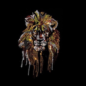 May include: A lion head graphic composed of numerous small, reflective rhinestones in shades of gold, amber, orange, and clear white. The design features a detailed mane and facial features, set against a solid, deep black background.