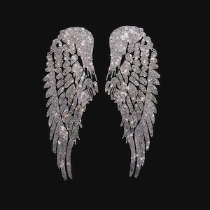 May include: A pair of symmetrical angel wings composed of numerous small, clear, reflective rhinestones arranged in a detailed feather pattern. The wings are positioned side-by-side, creating a sharp contrast against the solid black background.