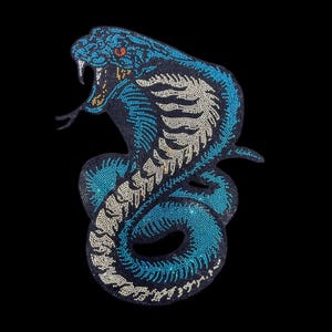 May include: A decorative iron-on patch featuring a coiled cobra snake design. The snake is crafted with blue, white, and yellow rhinestones, showing an open mouth with fangs, a forked tongue, and a detailed scale pattern across its body.