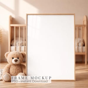 May include: A vertical rectangular wooden picture frame with a blank white center, positioned next to a light brown plush teddy bear. The frame features a simple light wood border, and the text FRAME MOCKUP PSD Instant Download is visible.