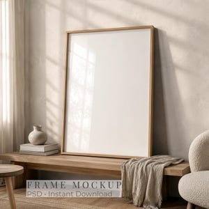 May include: A vertical rectangular wooden picture frame with a blank white center, positioned on a wooden bench. The frame features a light-toned wood finish and a clean, simple design, providing a neutral display area for artwork or photography.