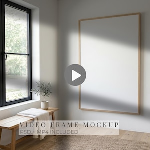 Puede incluir: Un marco rectangular vertical grande con borde de madera clara montado en una pared blanca. El marco muestra una superficie blanca vacía. El texto superpuesto dice VIDEO FRAME MOCKUP PSD + MP4 INCLUDED. Un icono de play está centrado.