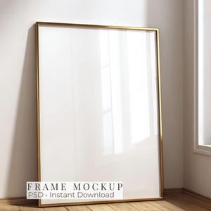 May include: A vertical rectangular picture frame with a thin metallic gold border and a clear glass front. The frame is empty, displaying a blank white interior surface. The text "FRAME MOCKUP PSD • Instant Download" is printed at the bottom.
