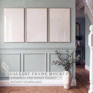 May include: Three vertical rectangular frames with thin light-colored borders mounted on a pale green paneled wall. Below the frames sits a beige ceramic vase containing leafy branches. Text reads: GALLERY FRAME MOCKUP 3 FRAMES PSD SMART OBJECT INSTANT DOWNLOAD.