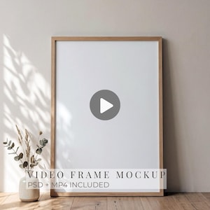 Pode incluir: Uma moldura retangular vertical de madeira com um centro branco vazio, apresentando um ícone de botão de reprodução no meio. O texto "VIDEO FRAME MOCKUP PSD + MP4 INCLUDED" está impresso na parte inferior da moldura.