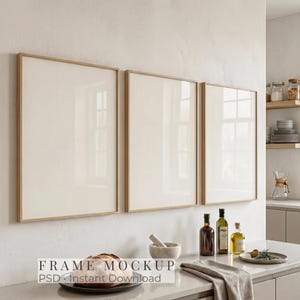 May include: Three framed art mockups with light wood frames hang on a white wall. Below, a kitchen counter displays olive oil bottles, a mortar and pestle, and a loaf of bread. The text "FRAME MOCKUP PSD Instant Download" is visible.
