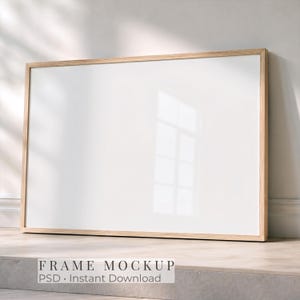 Op de afbeelding: Een horizontale rechthoekige fotolijst met een lichtgekleurde houten rand en een leeg wit midden. De lijst staat op een plat oppervlak en biedt een schone, lege ruimte voor kunstwerken of foto's, met de tekst FRAME MOCKUP.