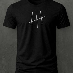 May include: A black short-sleeved t-shirt featuring a graphic design on the chest. The design consists of three vertical white lines crossed by a single diagonal white line, creating a tally mark style symbol centred on the front of the garment.