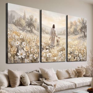Könnte beinhalten: Ein dreiteiliges Wandbild-Set im Stil eines Ölgemäldes. Die Szene zeigt eine Gestalt in einem langen Gewand, die mit einem kleinen Lamm durch ein Feld aus weißen und cremefarbenen Blumen geht, mit sanften Hügeln und Bäumen im Hintergrund.