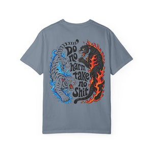 Könnte beinhalten: Ein schieferblaues T-Shirt mit einer Grafik auf der Rückseite, die einen grauen Tiger in blauem Wasser und einen schwarzen Tiger in orangefarbenen Flammen zeigt. Der Text "DO NO HARM TAKE NO SHIT" steht in einer schwarzen Schrift zwischen den Tigern.