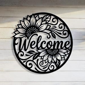 Peut inclure: Une enseigne murale circulaire en métal noir portant le mot Welcome en écriture cursive, entouré de découpes complexes de tournesols et de vignes tourbillonnantes. Le design est symétrique avec des motifs floraux en haut et en bas.