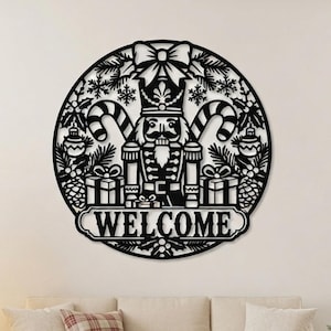 Pode incluir: Uma placa de parede circular em metal preto com uma figura detalhada de quebra-nozes ao centro, ladeada por bengalas doces, caixas de presente e ramos de pinheiro. A palavra WELCOME está exibida num banner na parte inferior do design.