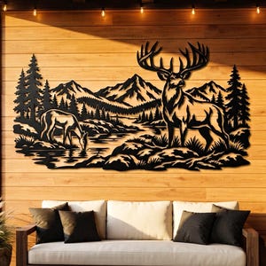 Puede incluir: Una pieza de arte mural de metal negro que presenta la silueta detallada de un gran ciervo con astas cerca de un ciervo más pequeño bebiendo de un arroyo, con un fondo de pinos y picos montañosos, creando una escena inspirada en la naturaleza.