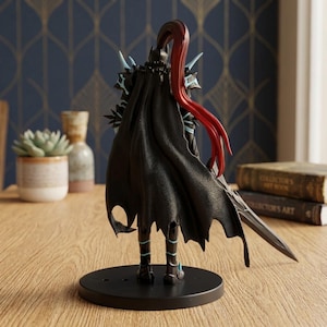 May include: A black figurine of a warrior with a flowing cape and red hair. The figure is posed with a sword and stands on a black circular base. The warrior's armor has blue accents.