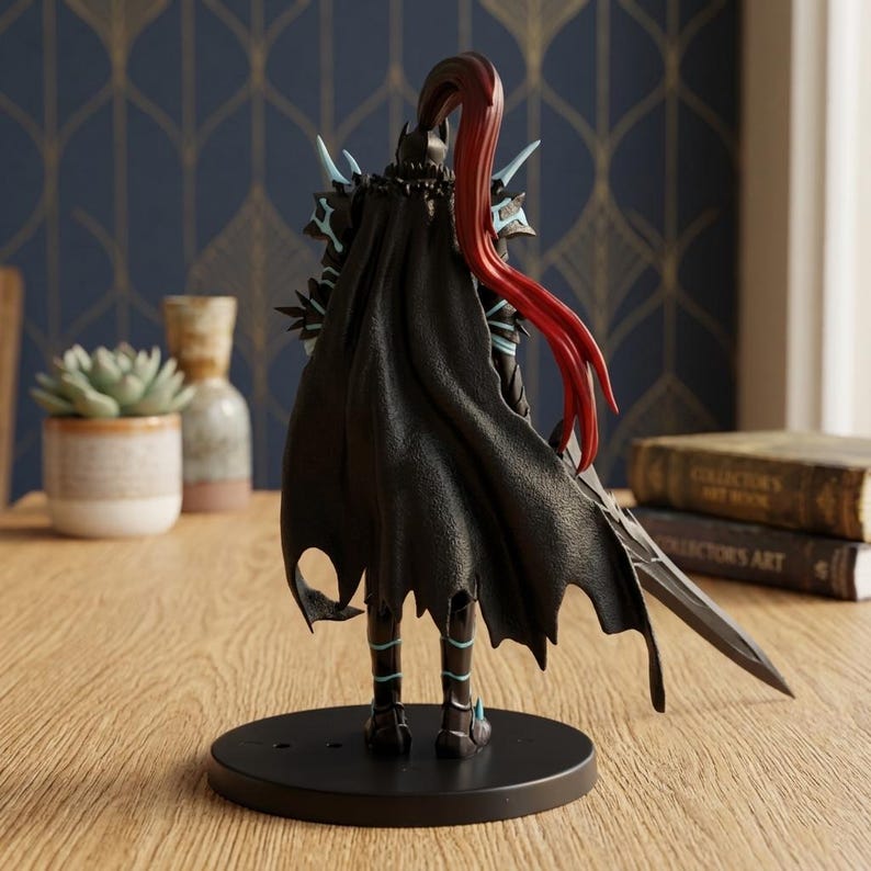 May include: A black figurine of a warrior with a flowing cape and red hair. The figure is posed with a sword and stands on a black circular base. The warrior's armor has blue accents.