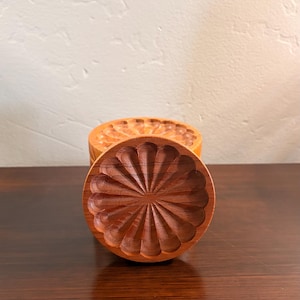 Puede incluir: Una taza de cerámica blanca con un asa negra y el texto "But First, Coffee" en negrita negra. La taza se encuentra sobre un fondo neutro, resaltando su diseño simple.