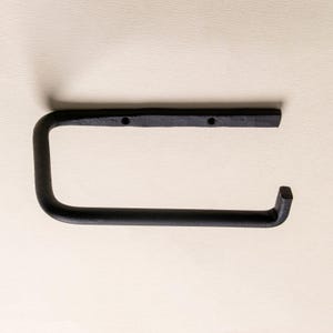 May include: A matte black metal toilet paper holder with a U-shaped design. The mounting bar features two pre-drilled holes for installation, and the horizontal arm extends outward to hold a roll, ending in a slightly upturned square tip.
