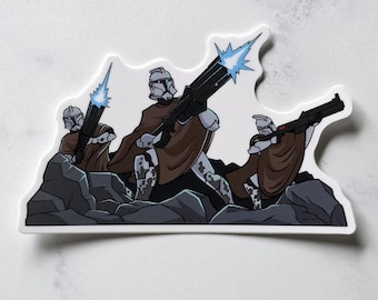 May include: A die-cut sticker featuring three white armoured soldiers wearing brown ponchos and helmets, positioned behind dark grey rocks. Each soldier holds a black blaster rifle, with two of the weapons emitting bright blue muzzle flashes.