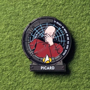 Puede incluir: Un pin de esmalte negro y plateado con una imagen de Jean-Luc Picard de Star Trek. El pin incluye el texto "TO BOLDLY GO WHERE NO ONE HAS GONE BEFORE" y el nombre "PICARD".