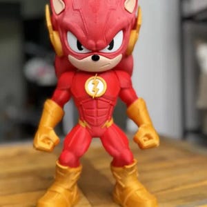 May include: A red and gold figurine of a hybrid character, combining elements of Sonic the Hedgehog and The Flash. The figure has a red body, gold boots and gloves, and a lightning bolt emblem on the chest.