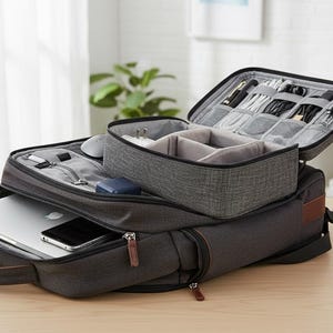 May include: A grey and black backpack with an open top compartment revealing organised storage for electronics and accessories. A laptop and smartphone are visible in the main compartment. A smaller grey organiser sits on top.