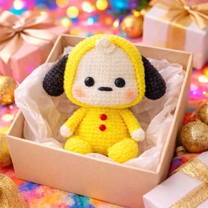 May include: A handmade yellow crochet doll with a white face, black eyes, and black ears, sitting in a beige box. The doll has two red buttons and is surrounded by gift boxes and colorful bokeh lights.