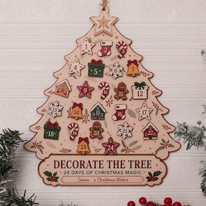 May include: A wooden Christmas tree-shaped advent calendar with 24 numbered icons including stars, stockings, gifts, and gingerbread men. The base features the text "DECORATE THE TREE", "24 DAYS OF CHRISTMAS MAGIC", and "Emma's Christmas Wishes".