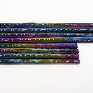 May include: A set of ten iridescent glass rods, each with a textured surface. The rods are arranged in a stack, with the ends of the rods aligned. The rods are a mix of blue, purple, green, and gold colors.
