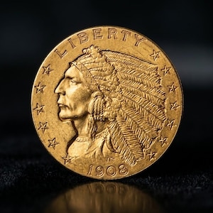 May include: A gold coin featuring a profile of a Native American in a feathered headdress, with the word "LIBERTY" and stars. The year "1908" is inscribed. The coin is set against a dark background.