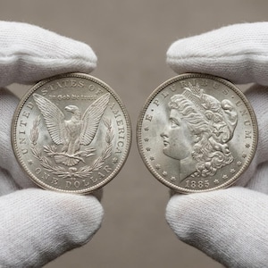 Puede incluir: Una taza de cerámica blanca con un asa negra y el texto "But First, Coffee" en negro, con una fuente de estilo manuscrito. La taza está sobre una superficie blanca.