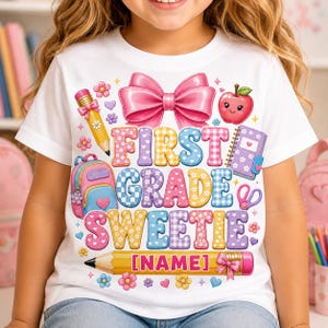 May include: A white t-shirt featuring a colourful graphic with the text FIRST GRADE SWEETIE and [NAME] on a yellow pencil. The design includes a large pink bow, a red apple, a pink backpack, a purple notebook, scissors, and various small flowers.