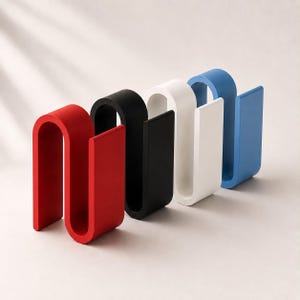 May include: A set of four S-shaped organizers in red, black, white, and blue. Each organizer features a continuous, curved design with a flat base and a vertical slot, providing a structured form for holding items in a clean, upright position.