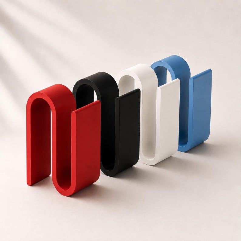 May include: A set of four S-shaped organizers in red, black, white, and blue. Each organizer features a continuous, curved design with a flat base and a vertical slot, providing a structured form for holding items in a clean, upright position.