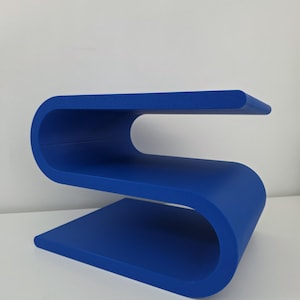 May include: A vibrant blue side table featuring a continuous S-shaped design with two horizontal surfaces. The structure is formed from a single piece of material that curves to create an upper shelf and a lower base, providing a sleek profile.