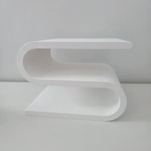 May include: A white side table featuring a continuous S-shaped design with a flat top surface, a middle shelf, and a flat base. The structure is formed from a single piece of material with smooth, rounded curves connecting each horizontal level.