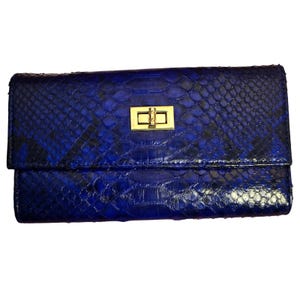 May include: A rectangular wallet featuring a vibrant blue and black snakeskin-patterned texture. The front flap is secured with a polished gold-tone rectangular turn-lock closure centered on the upper portion of the wallet's exterior surface.