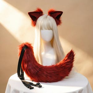 Pode incluir: Um conjunto de orelhas de animal em pele sintética vermelho-escura numa bandolete e uma cauda longa e curva em pele sintética a condizer. A cauda possui uma correia preta ajustável com fivelas de plástico. Apresentado num manequim.